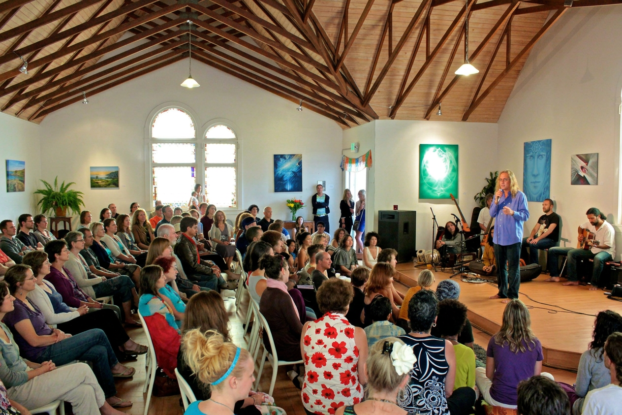 Prasad Paul Duffy speaking to a gathering Prasad Paul Duffy speaking into a microphone before an audience at a spiritual gathering